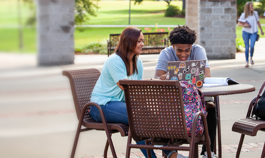 white female student and black male student sitting at an outdoor table reviewing notes
